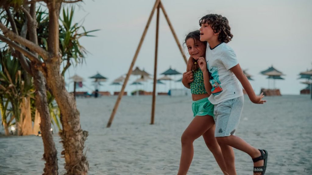 Two children enjoy a playful walk on a sandy beach, capturing summer fun.