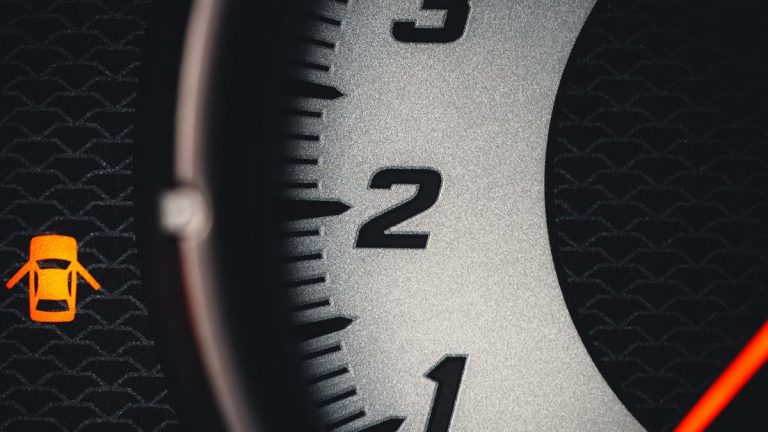 Detailed close-up of a car tachometer featuring a warning icon, focusing on the numbers with modern design elements.